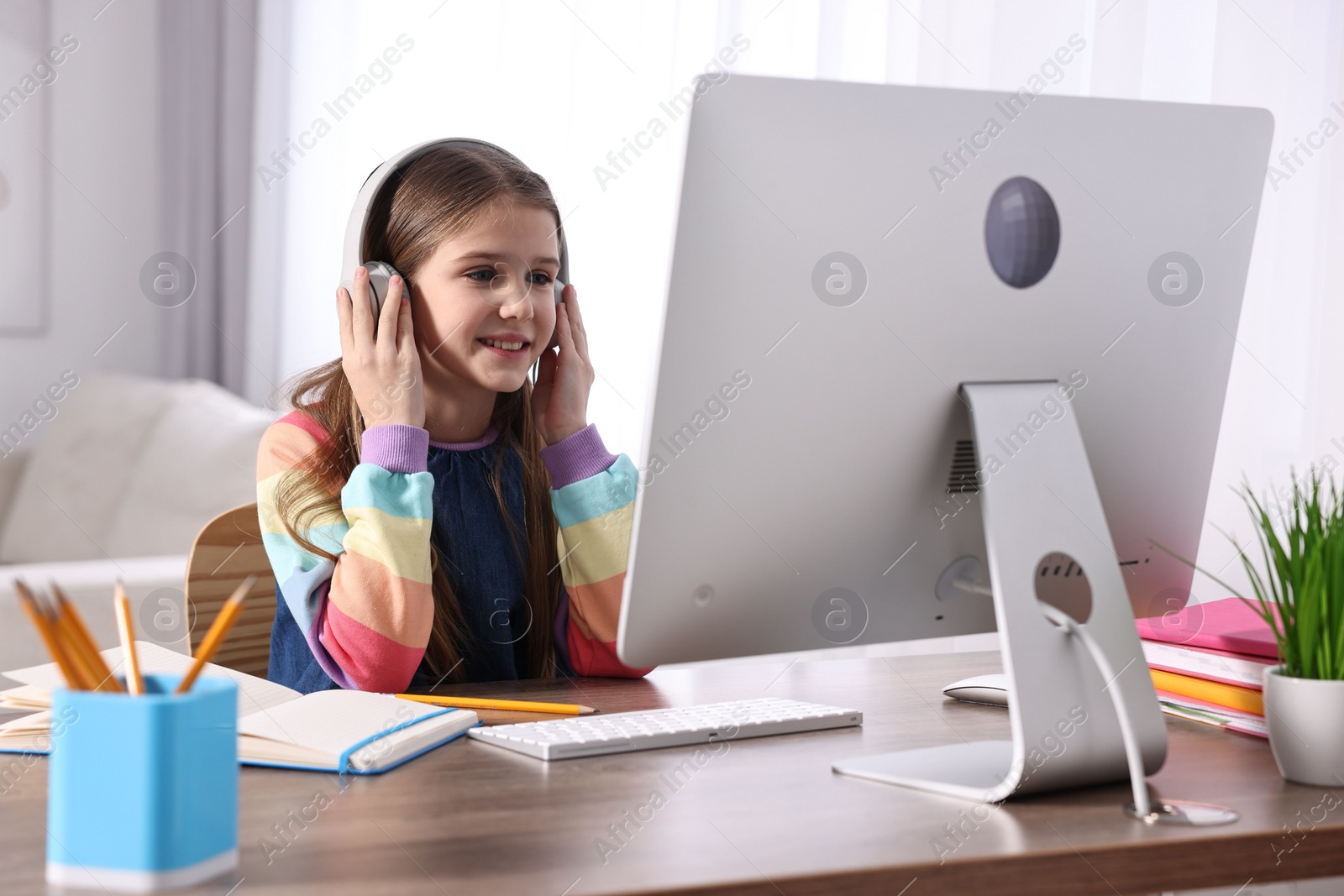 Photo of E-learning. Cute girl using computer and headphones during online lesson at table indoors