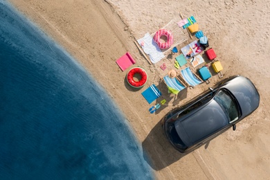 Car and beach accessories on sand near river, aerial view. Summer trip