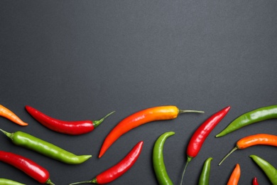 Different colorful chili peppers on black background, flat lay. Space for text