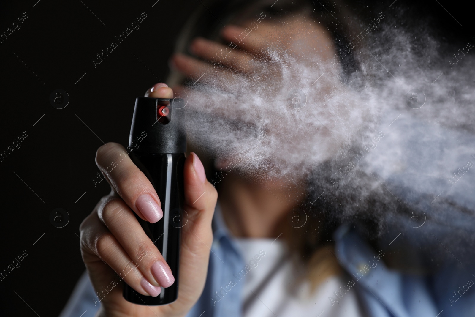 Image of Young woman covering eyes with hand and using pepper spray on black background