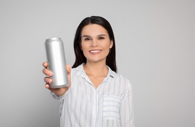 Photo of Beautiful young woman holding tin can with beverage on light grey background. Space for text