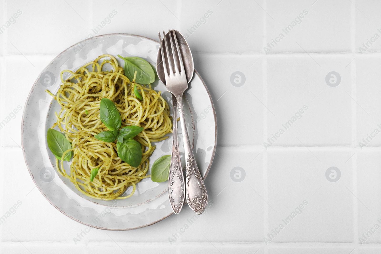 Photo of Delicious pasta with pesto sauce and basil served on white tiled table, flat lay