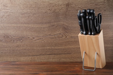 Holder with set of knives on wooden table. Space for text