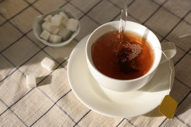 Pouring hot water into cup with tea bag on table, above view