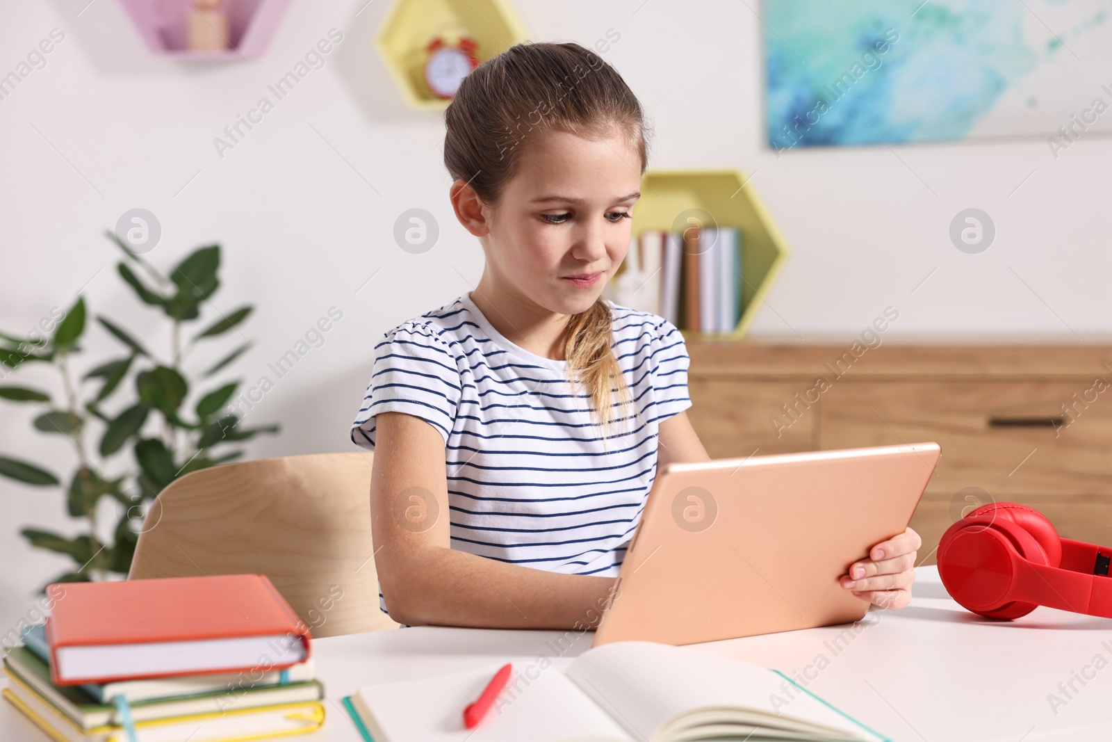 Photo of E-learning. Cute girl using tablet for studying online at table indoors