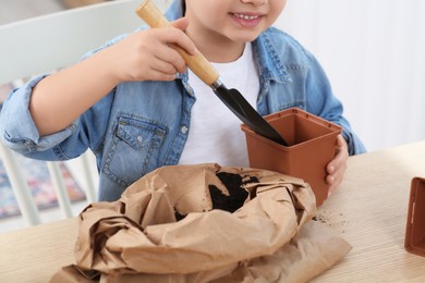 Little girl planting seedling into pot at wooden table indoors, closeup