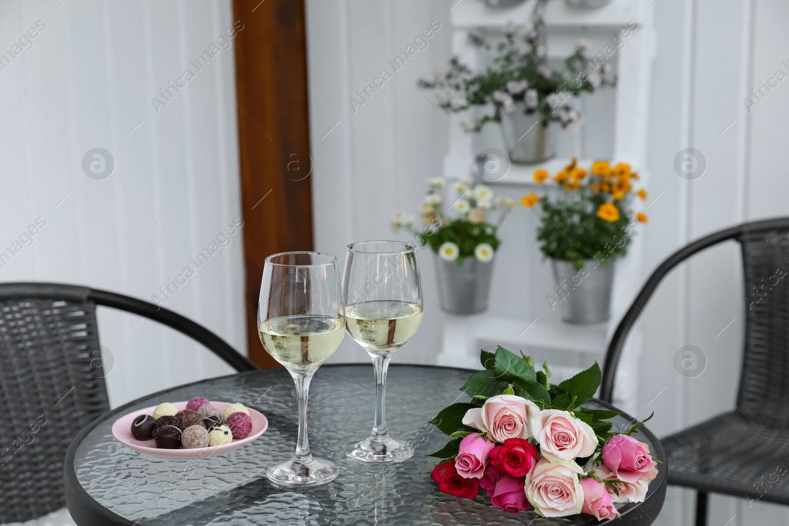 Photo of Bouquet of roses, glasses with wine and candies on glass table on outdoor terrace