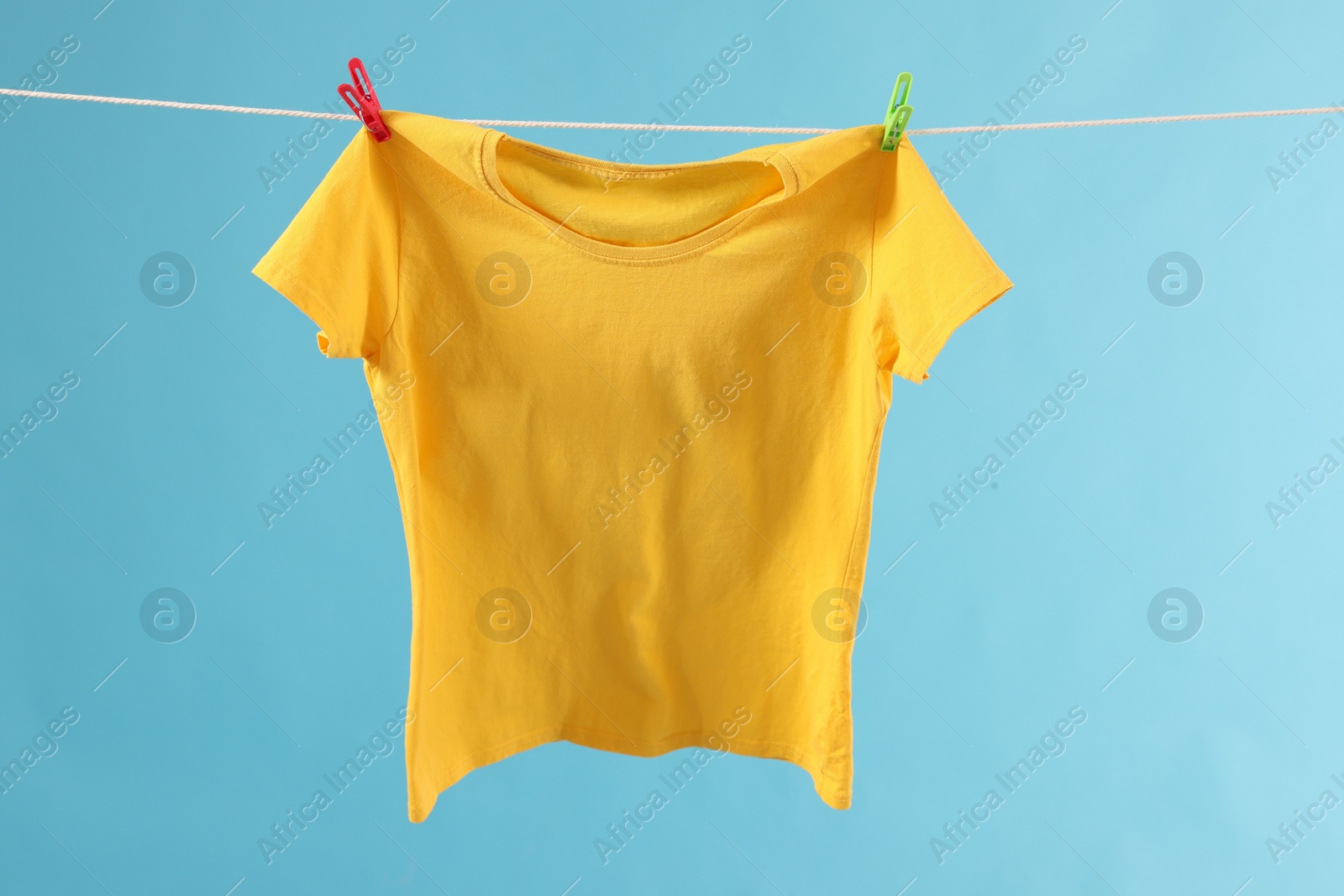 Photo of One yellow t-shirt drying on washing line against light blue background