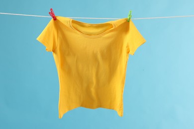 Photo of One yellow t-shirt drying on washing line against light blue background