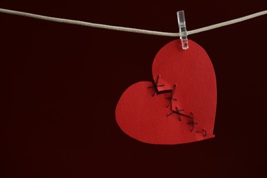 Photo of Broken heart. Torn red paper heart sewed with thread on rope against burgundy background, space for text