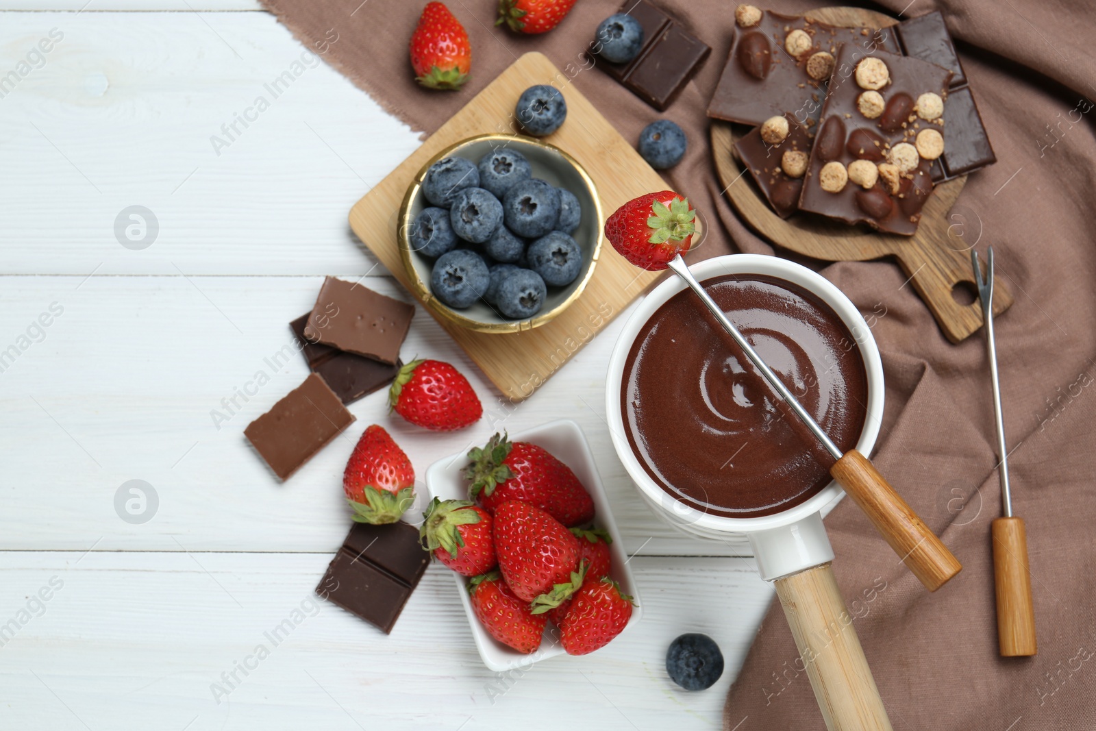 Photo of Fondue pot with chocolate, different berries and forks on white wooden table, flat lay. Space for text