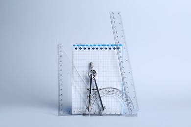 Photo of Triangle, notebook, protractor and compass on white background