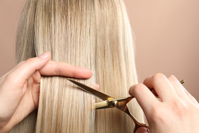 Photo of Hairdresser cutting client's hair with scissors on beige background, closeup