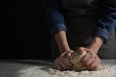 Photo of Making bread. Woman kneading dough at table on dark background, closeup. Space for text