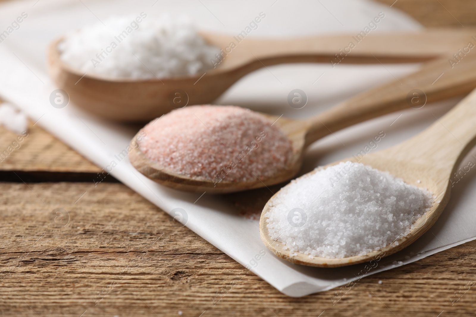 Photo of Different salt in spoons on wooden table, closeup