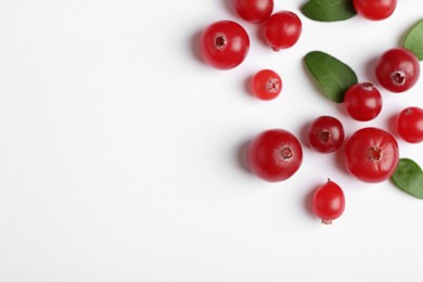 Photo of Fresh ripe cranberries and green leaves on white background, flat lay. Space for text