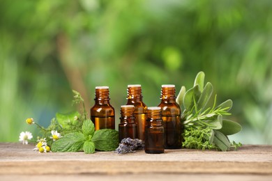 Bottles with essential oils and plants on wooden table against blurred green background. Space for text