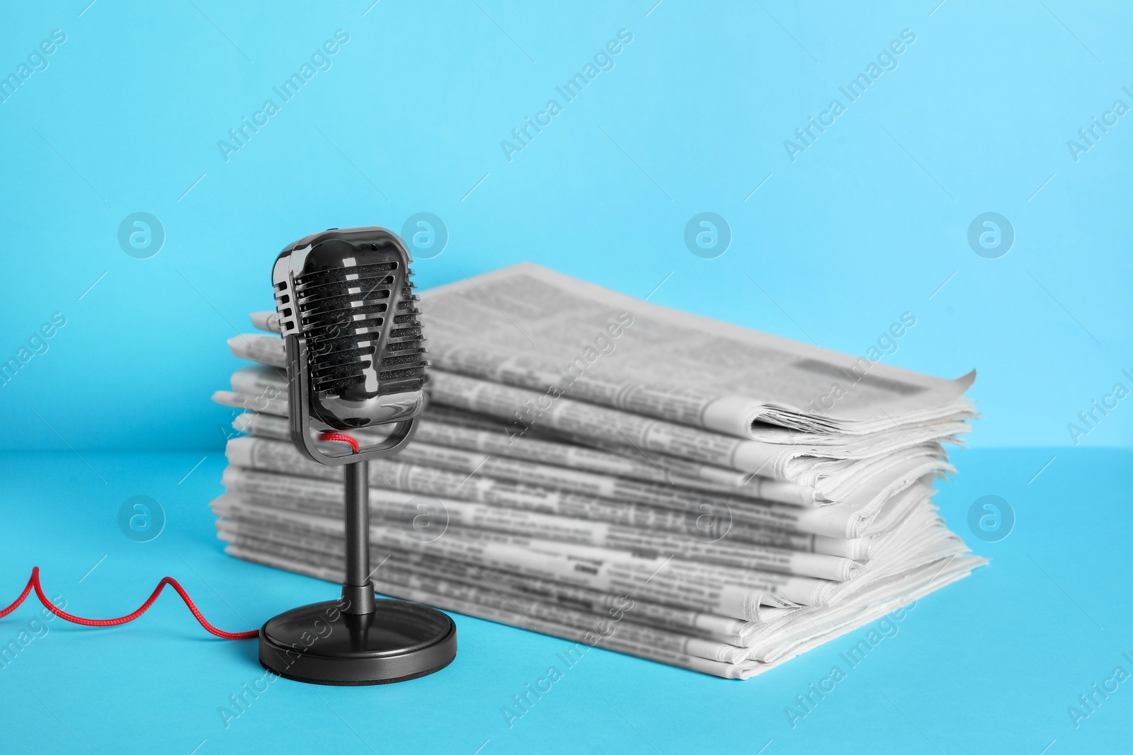 Photo of Newspapers and vintage microphone on light blue background. Journalist's work