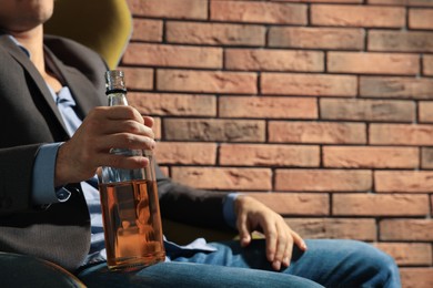 Photo of Addicted man with bottle of alcoholic drink near red brick wall, closeup. Space for text