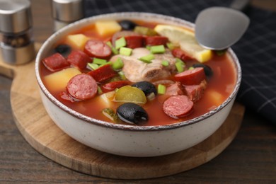 Meat solyanka soup with thin dry smoked sausages in bowl on wooden table, closeup