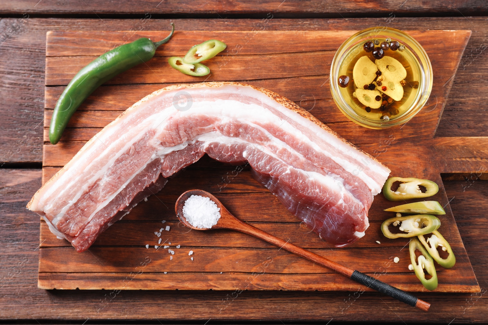 Photo of Piece of raw pork belly, green chili pepper and oil with spices on wooden table, top view