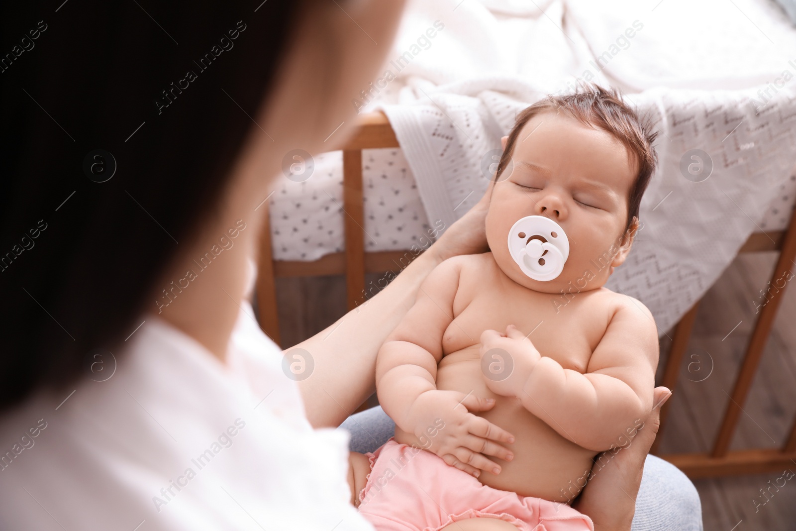 Photo of Mother holding her cute little baby with pacifier at home, closeup