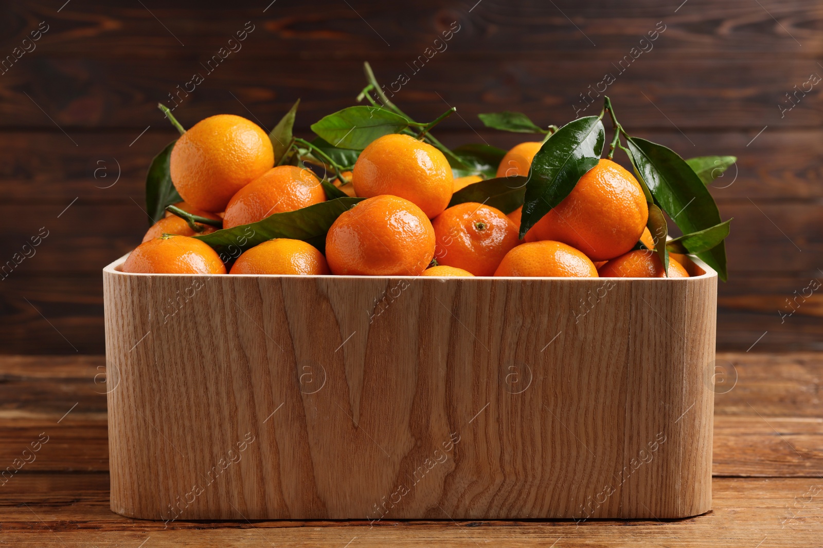 Photo of Fresh tangerines with green leaves in crate on wooden table