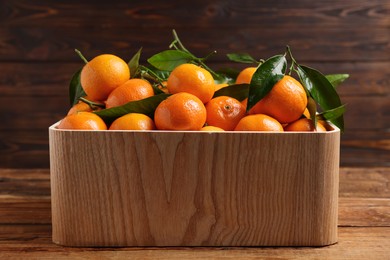Fresh tangerines with green leaves in crate on wooden table