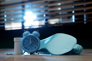 Photo of Alarm clock, sleeping mask and pills on table indoors. Insomnia treatment