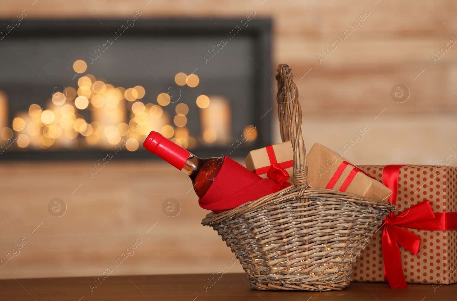 Photo of Wicker basket with bottle of wine and gift boxes on table in room. Space for text