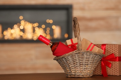 Photo of Wicker basket with bottle of wine and gift boxes on table in room. Space for text