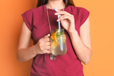 Photo of Young woman with mason jar of tasty lemonade on color background. Natural detox drink