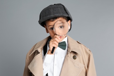 Little boy with magnifying glass playing detective on grey background