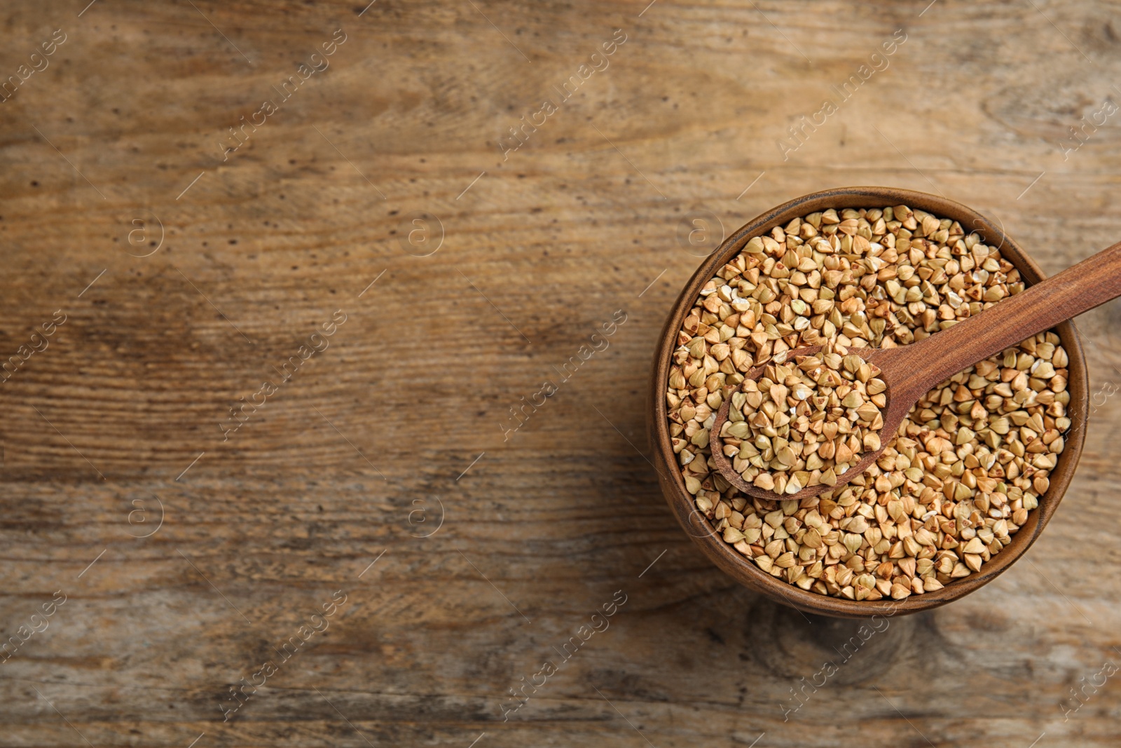 Photo of Uncooked green buckwheat grains in bowl on wooden table, top view. Space for text