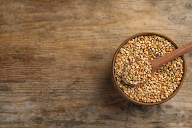 Photo of Uncooked green buckwheat grains in bowl on wooden table, top view. Space for text