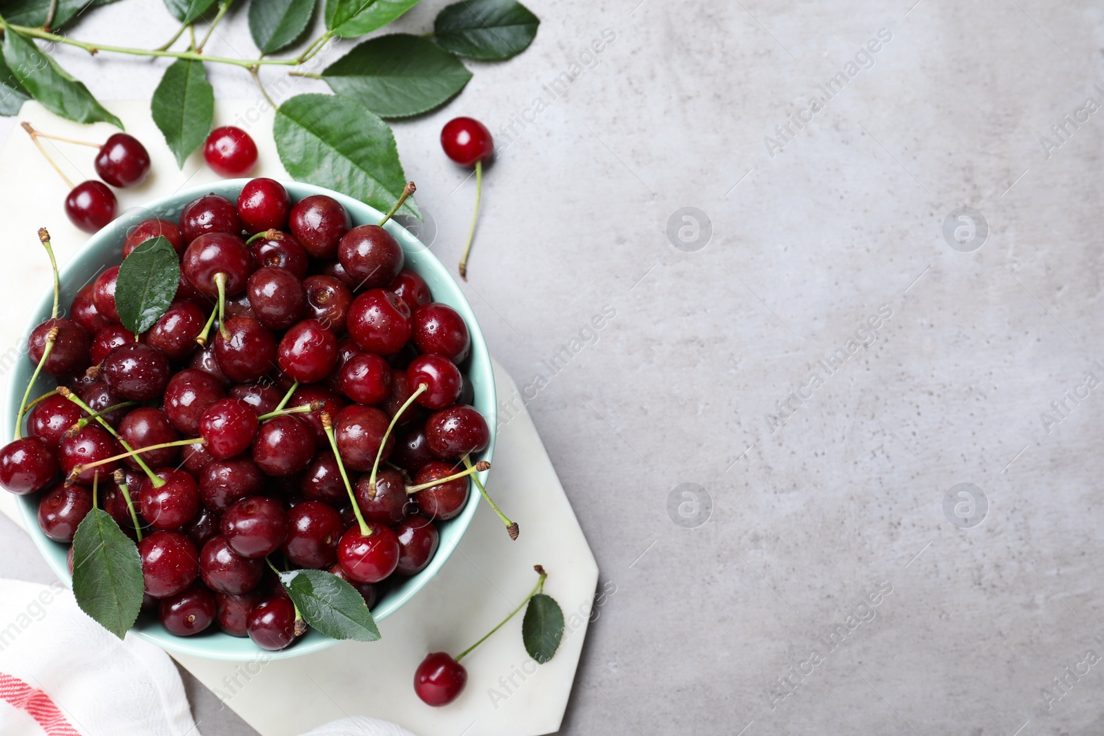 Photo of Sweet juicy cherries and leaves on grey table, flat lay. Space for text