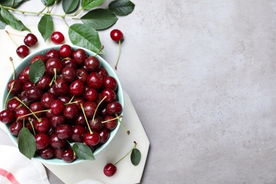 Sweet juicy cherries and leaves on grey table, flat lay. Space for text