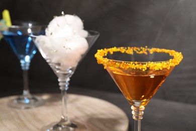 Tasty cotton candy cocktail and other alcoholic drinks in glasses on table against gray background, closeup
