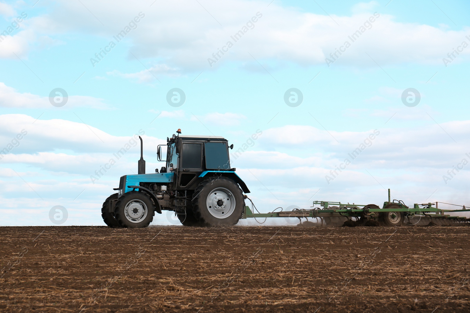 Photo of Tractor with planter cultivating field on sunny day. Agricultural industry