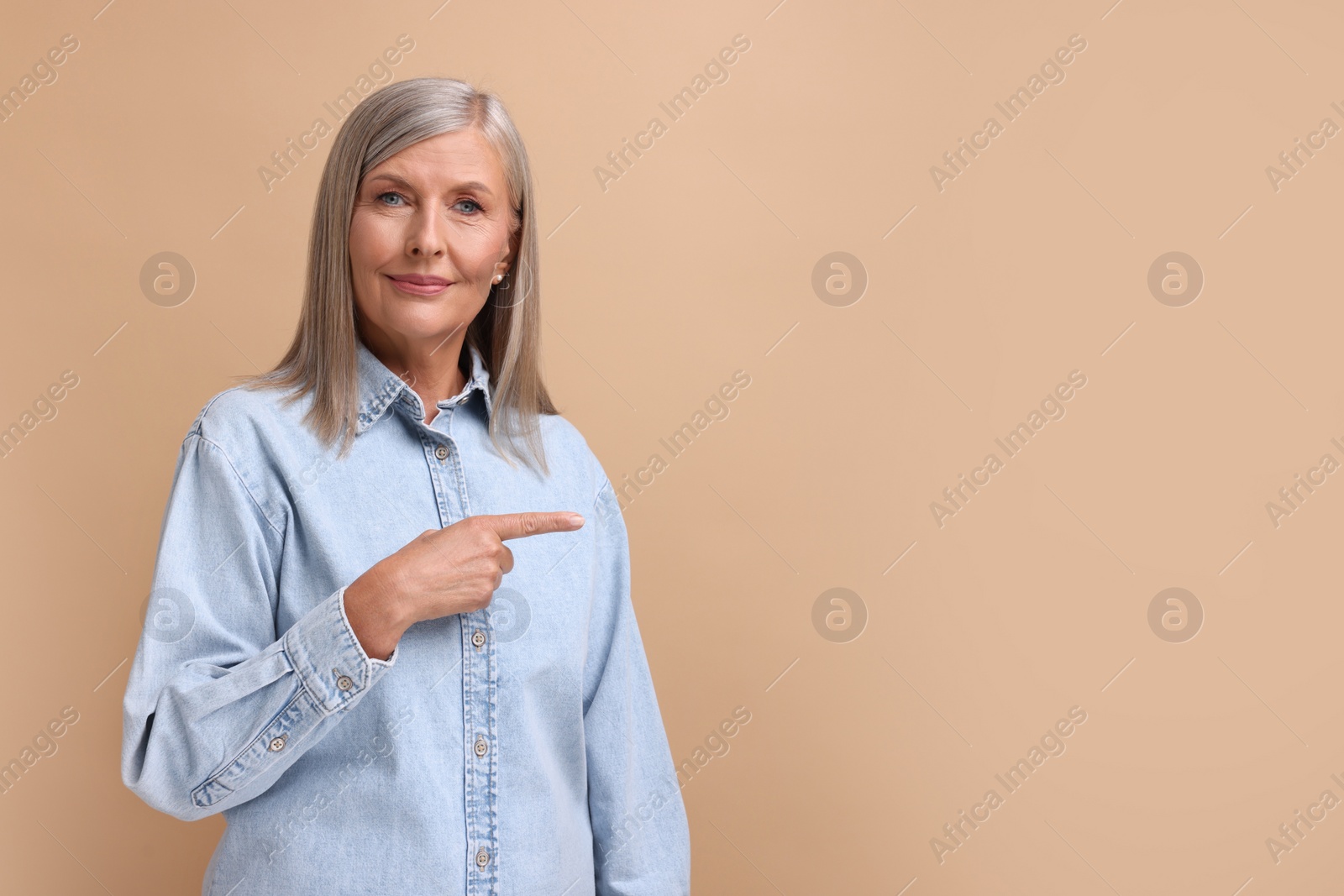 Photo of Portrait of beautiful middle aged woman pointing at something on beige background, space for text