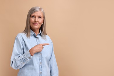 Photo of Portrait of beautiful middle aged woman pointing at something on beige background, space for text
