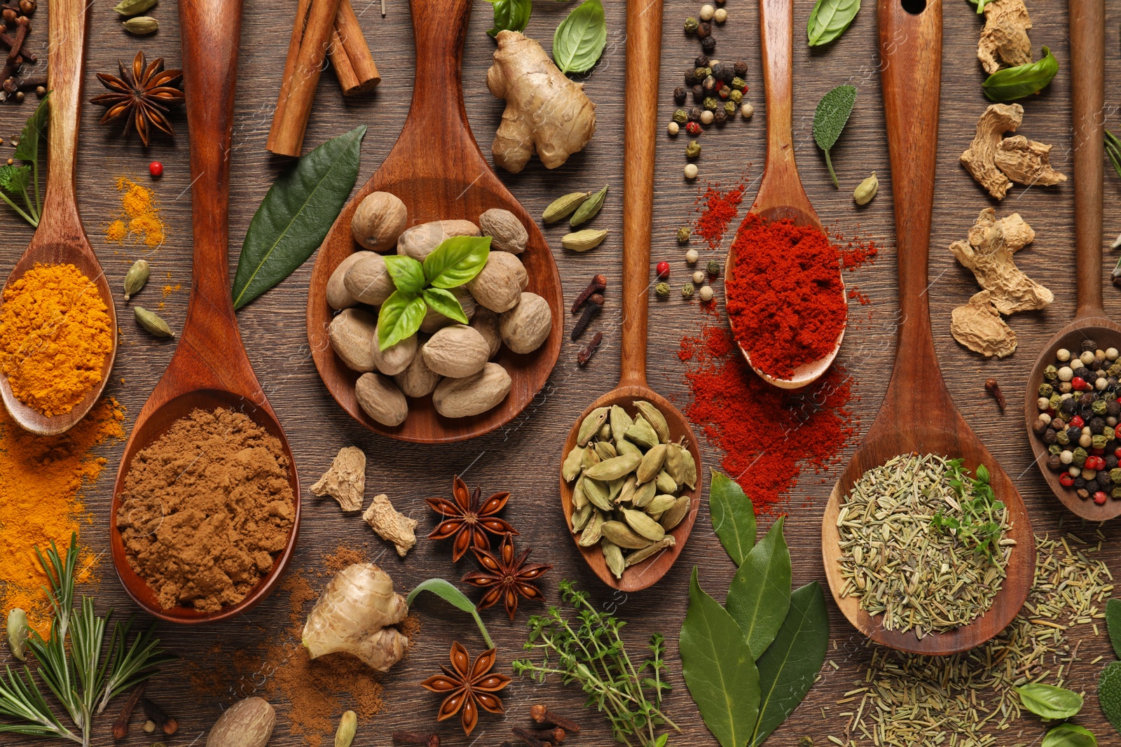 Photo of Different herbs and spices with spoons on wooden table, flat lay