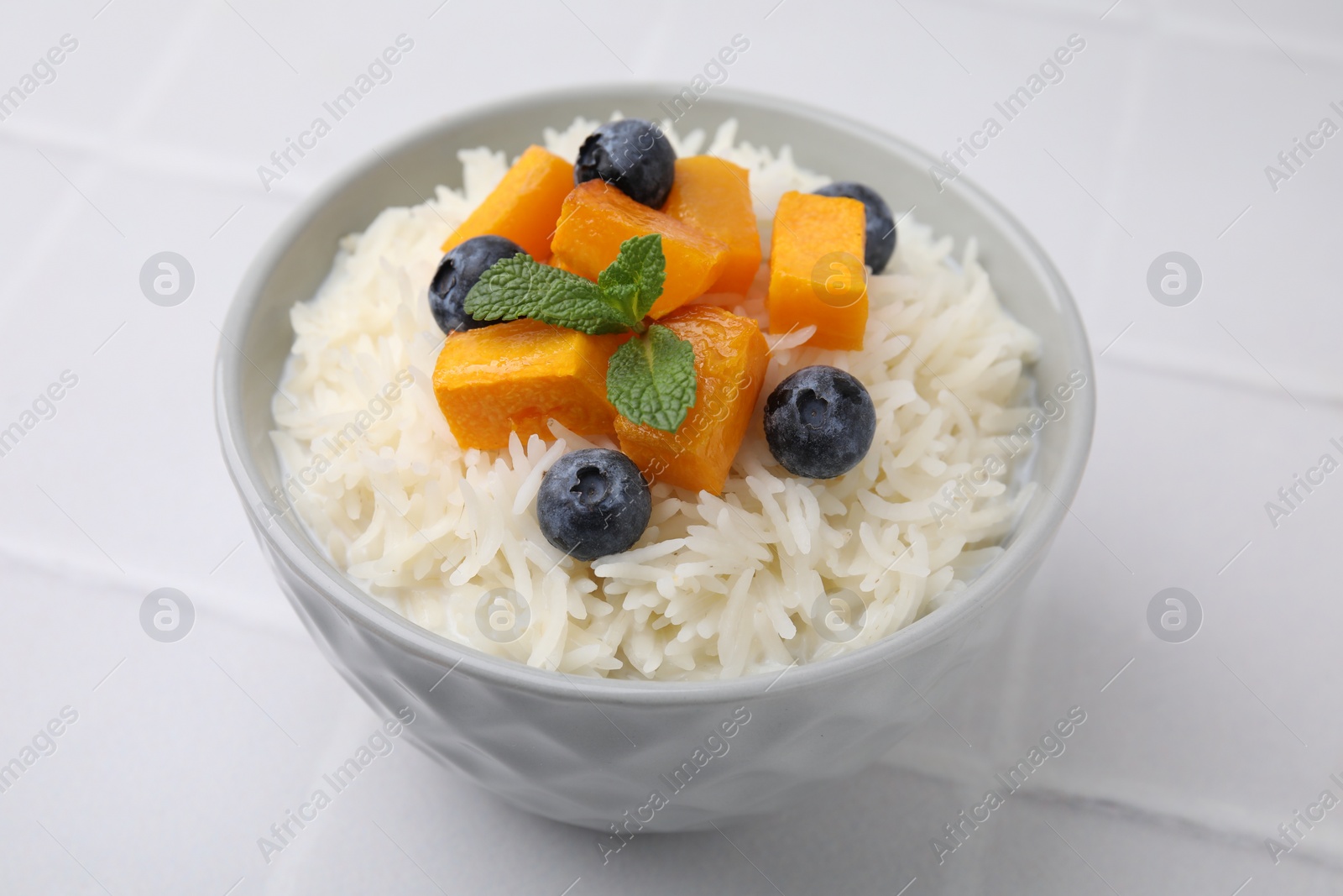 Photo of Bowl of delicious rice porridge with blueberries and pumpkin on white table, closeup