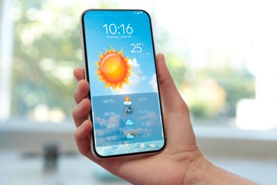 Woman checking weather using app on smartphone indoors, closeup. Data, sun and other illustrations on screen