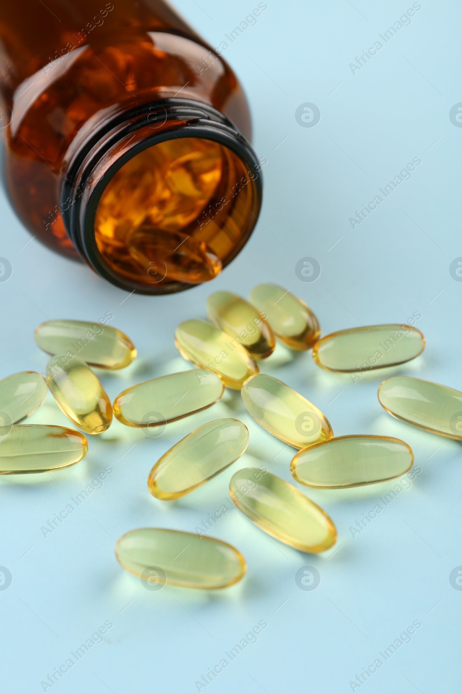 Photo of Bottle and vitamin capsules on light blue background, closeup