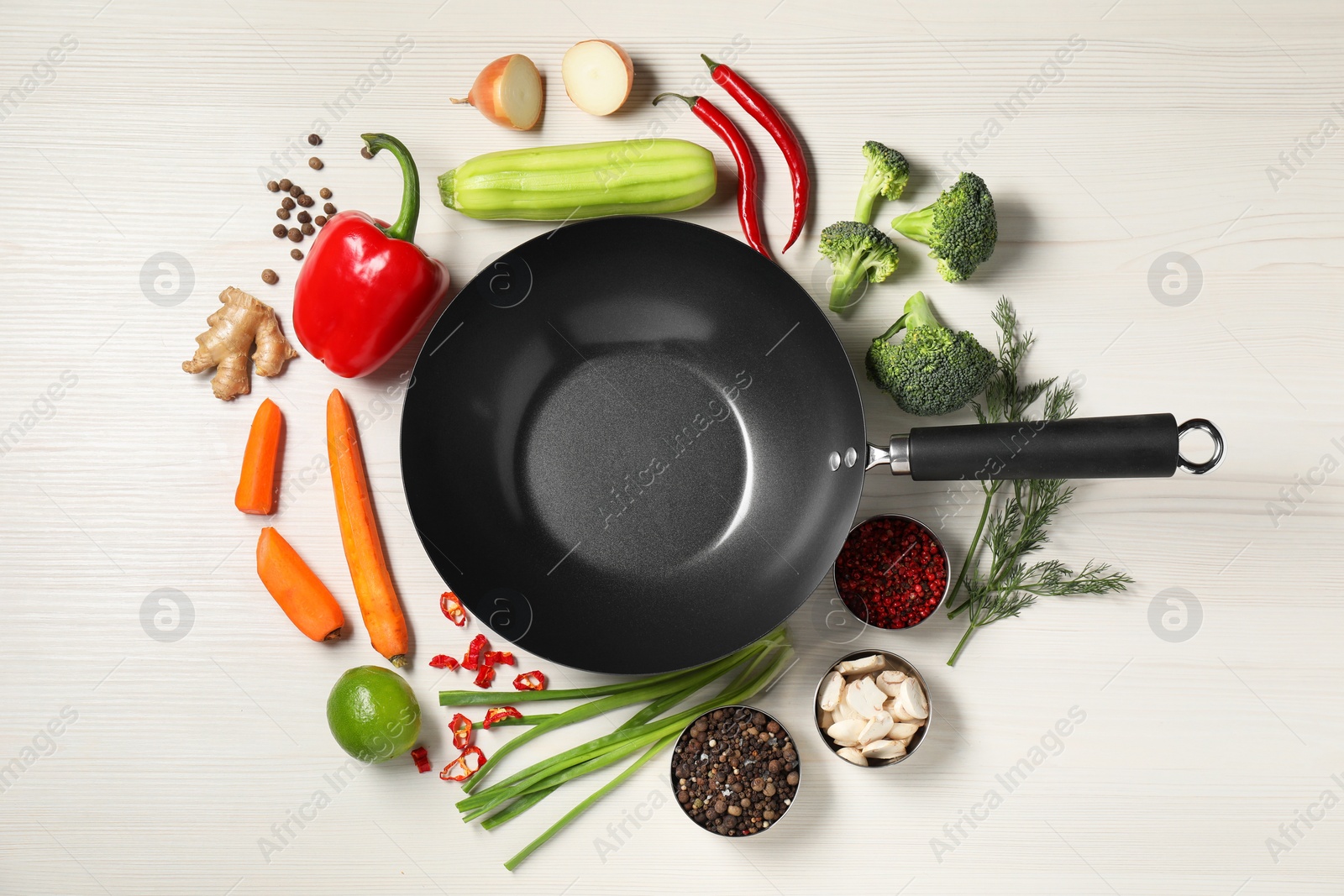 Photo of Empty iron wok surrounded by raw ingredients on white wooden table, flat lay