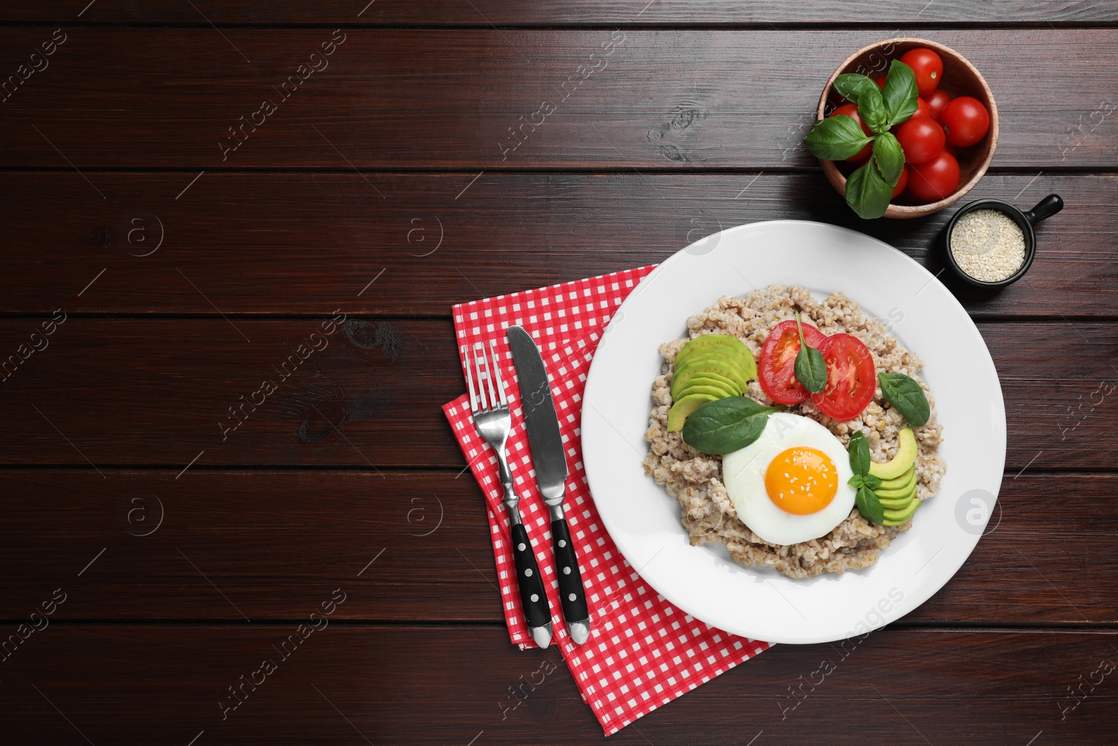 Photo of Delicious boiled oatmeal with fried egg, tomato and avocado served on wooden table, flat lay. Space for text