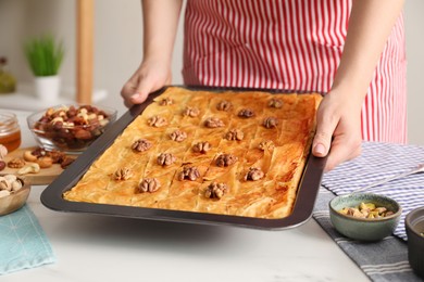 Photo of Woman holding baking pan of delicious baklava with walnuts above white table, closeup