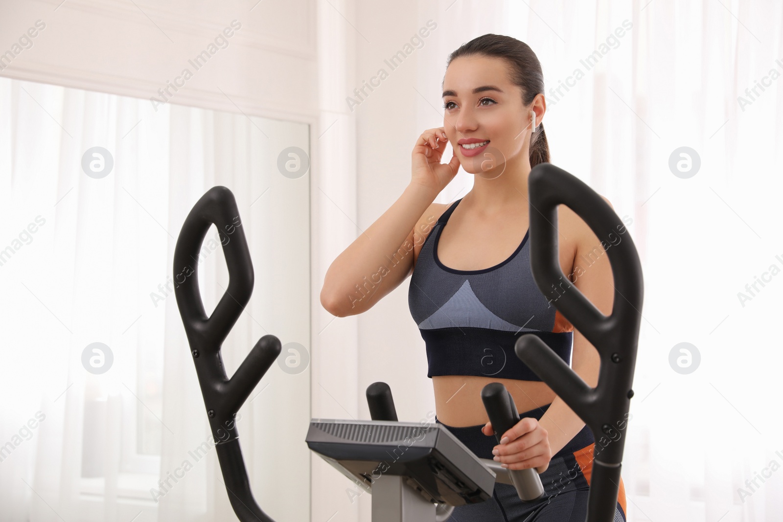 Photo of Young woman using modern elliptical machine indoors