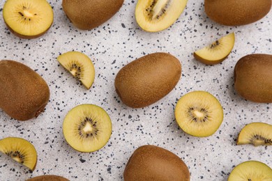 Photo of Whole and cut fresh kiwis on white table with pattern, flat lay